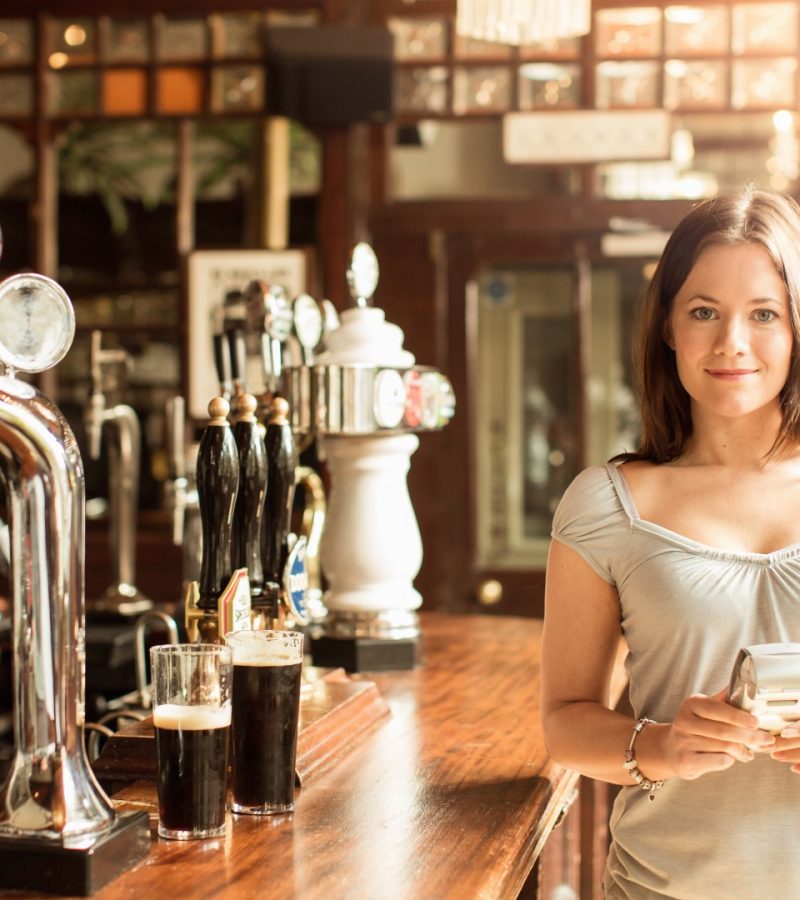 Mid adult woman working in public house holding chip and pin machine